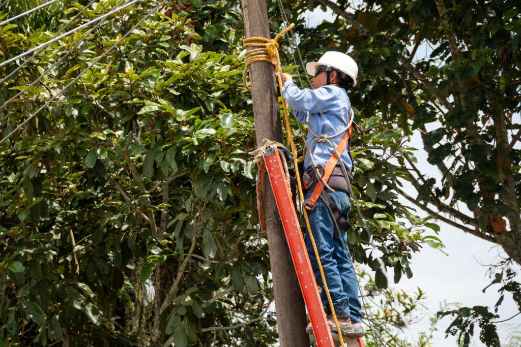 Male electrician wearing clothing, helmet and safety harness climbing on a light pole. Electrician at work.