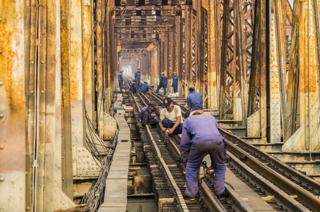 Group of anonymous male technicians in dirty uniforms building railroad together in city