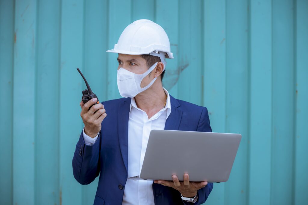 dock worker in suit and mask holding laptop talking on walkie