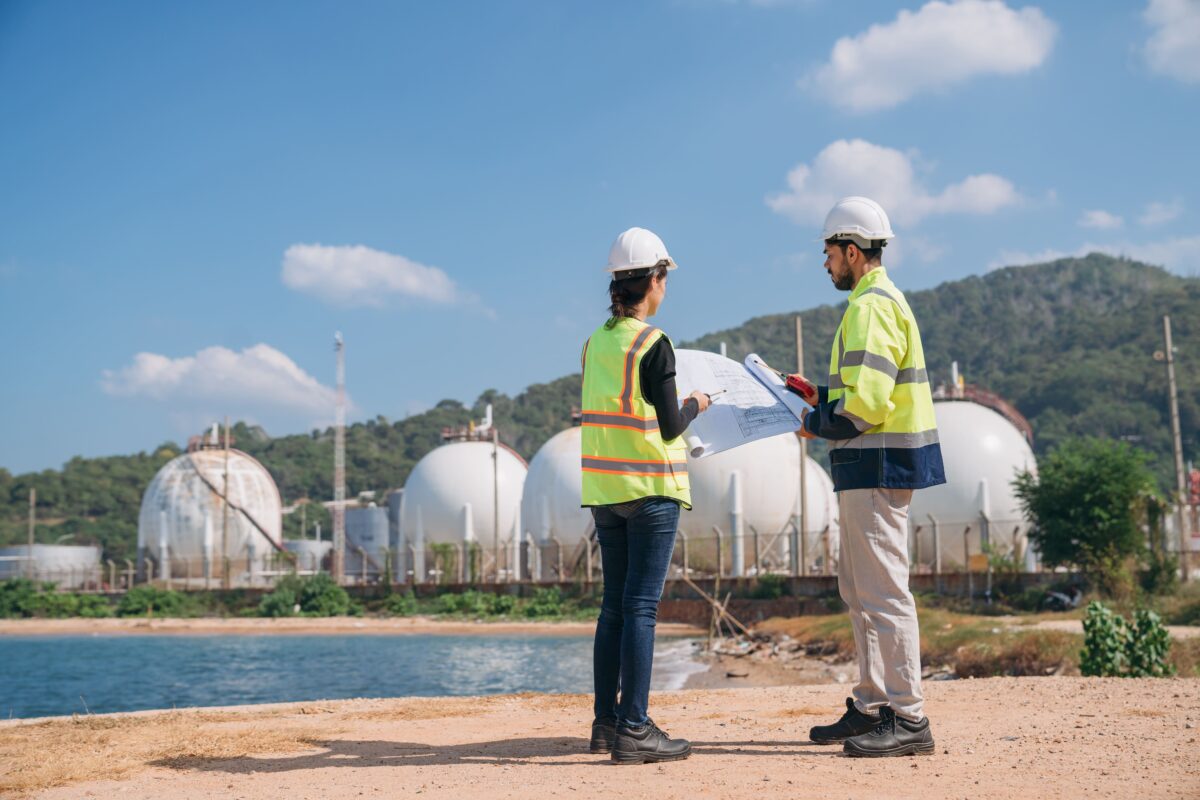 engineers with blue prints outside energy facility by the sea