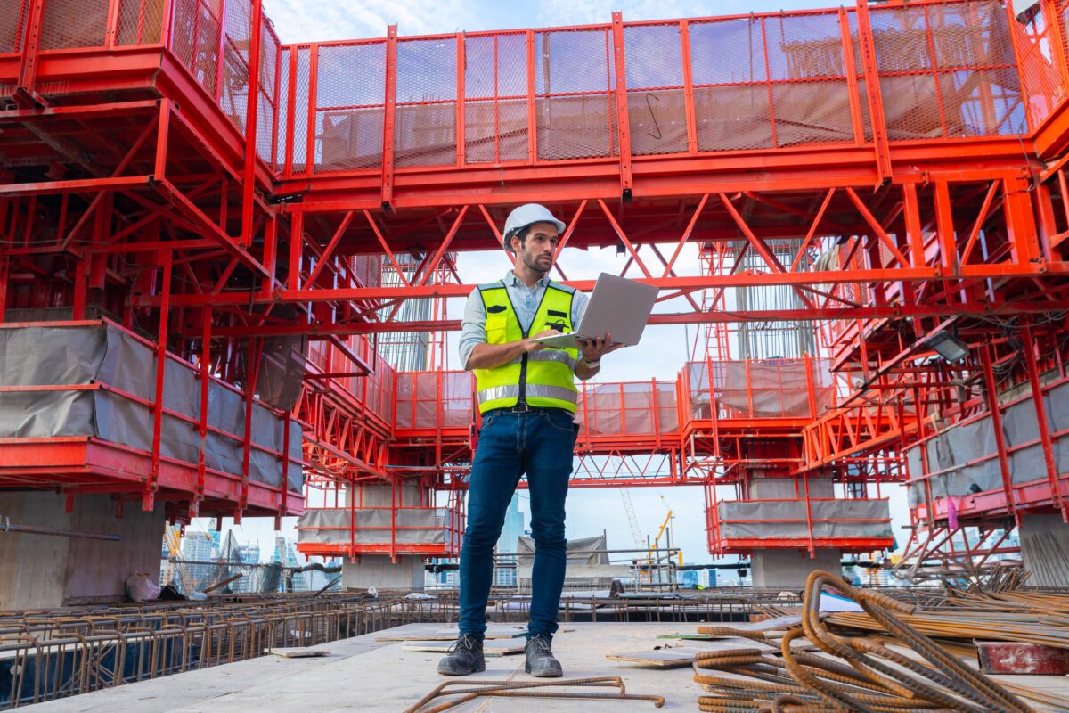 engineer in high-vis vest holding laptop standing on concrete floor at construction site