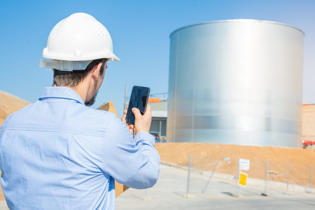 engineer with hard hat takes pic of oil tank