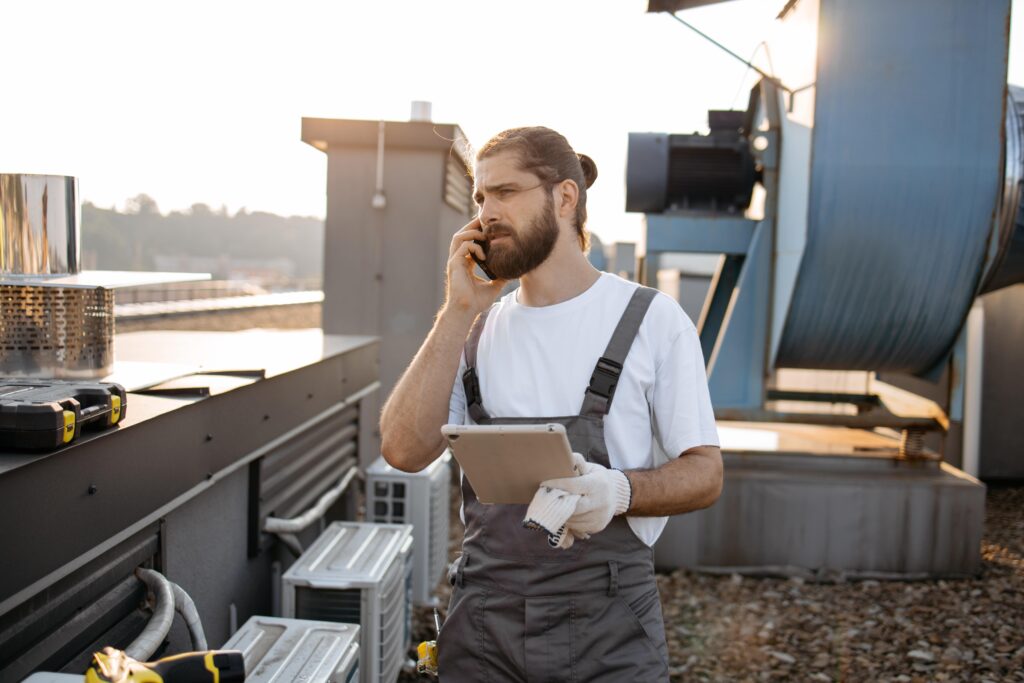 factory worker holding  tablet standing next to aircon units on rooftop 