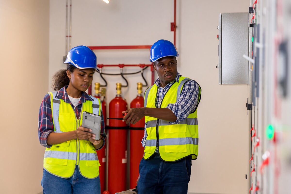male and female worker inspect work facility with fire extinguishers behind them