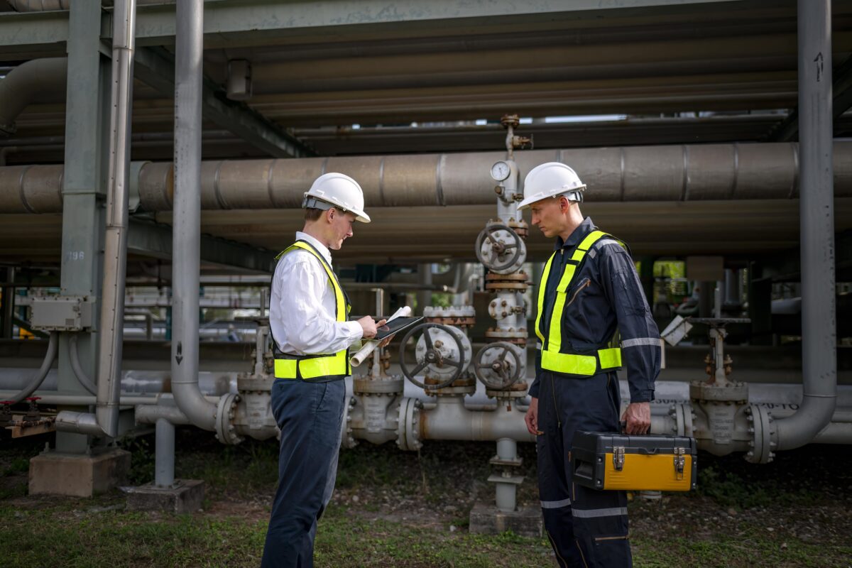 two engineers wear uniform standing among pipes