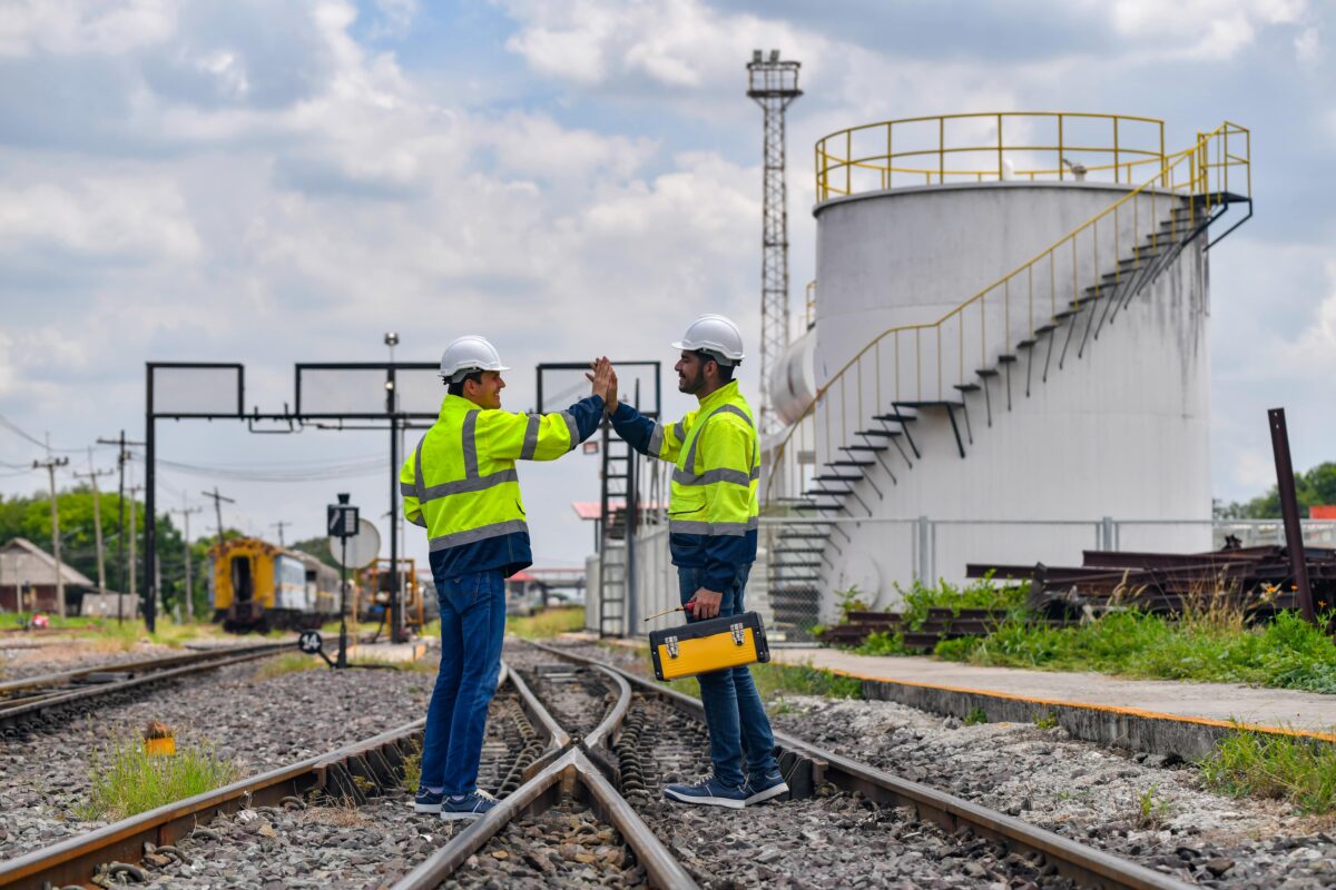 engineers standing on rail tracks with oil tanks in distance