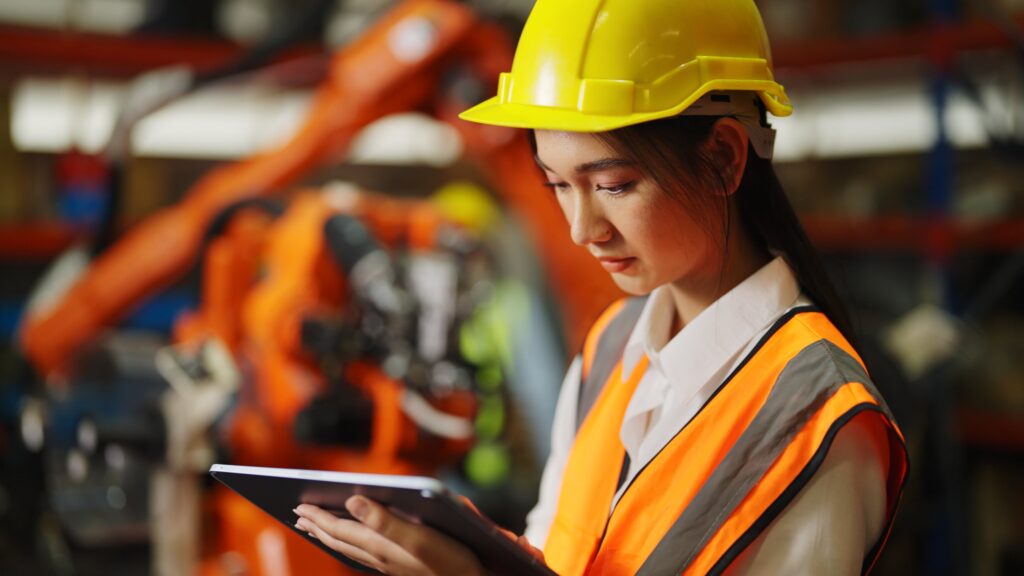 female engineer in safety clothing  writing on tablet in robot factory
